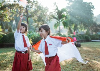 two indonesian school student holding flag during independence day. proud primary pupil with indonesia flag outdoor