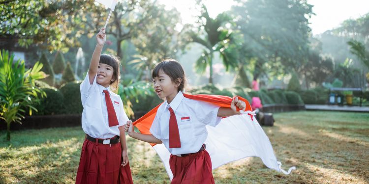 two indonesian school student holding flag during independence day. proud primary pupil with indonesia flag outdoor