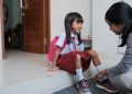 mother help her daughter to wear a shoes in the morning while preparing to go to school